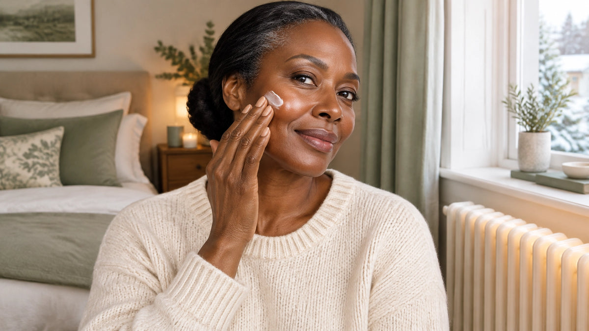 Black British woman applying moisturiser beside a softly glowing radiator in an elegant winter bedroom